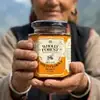 Himachali mountain elder holding Wholly Forest Himalayan Multiflora Raw Honey glass jar in both hands with mountain valley background