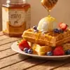 Golden raw honey being drizzled from wooden dipper onto warm Belgian waffles with vanilla ice cream and fresh berries