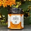Wholly Forest 350g hexagonal glass honey jar placed outdoors on stone slate surrounded by lush greenery and orange flowers