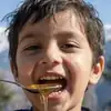 Smiling young boy tasting golden raw mountain honey dripping from a spoon with snowy Himalayan peaks in background